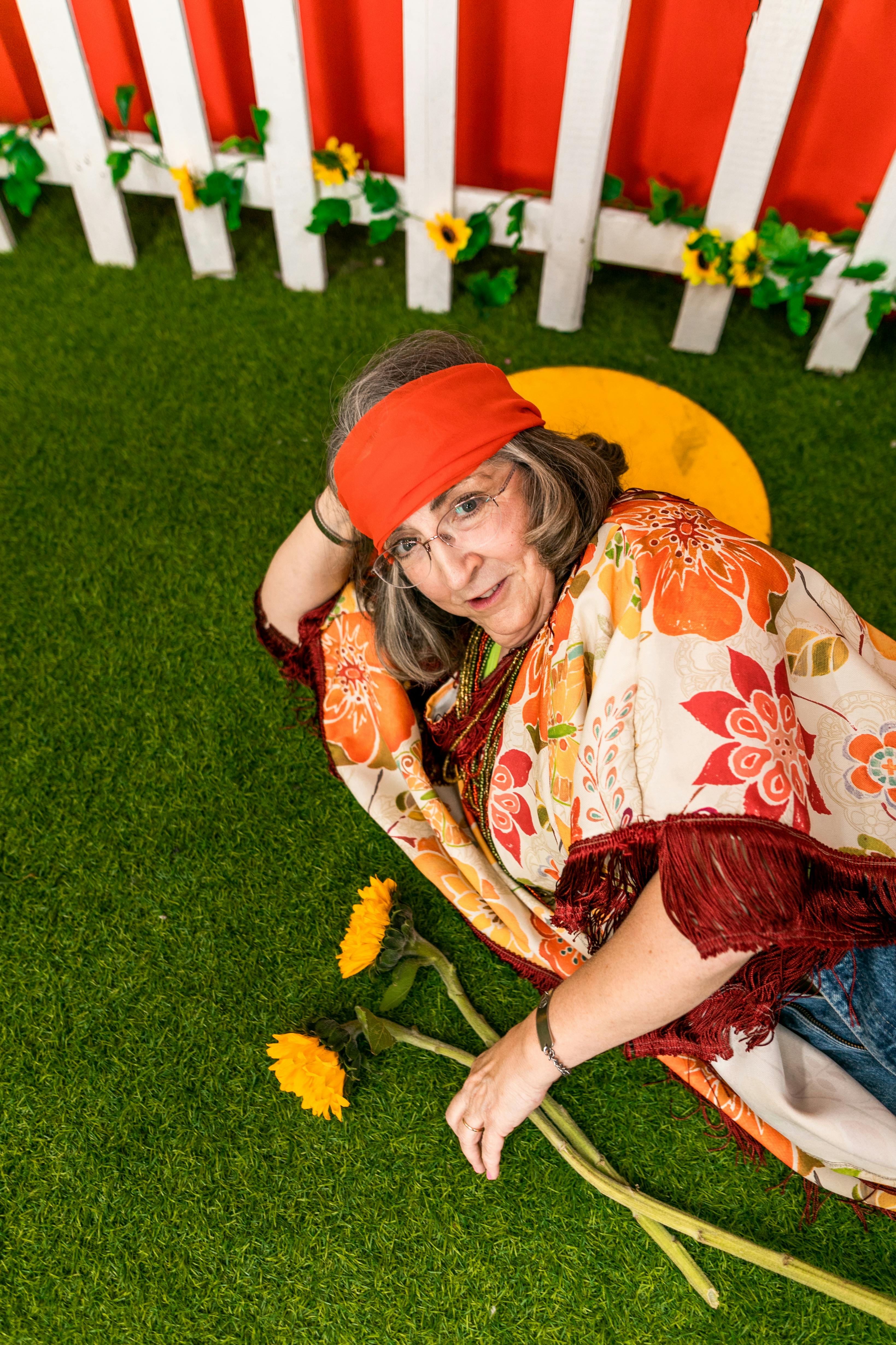 Senior woman dressed in hippie style enjoying a vibrant garden setting with flowers.