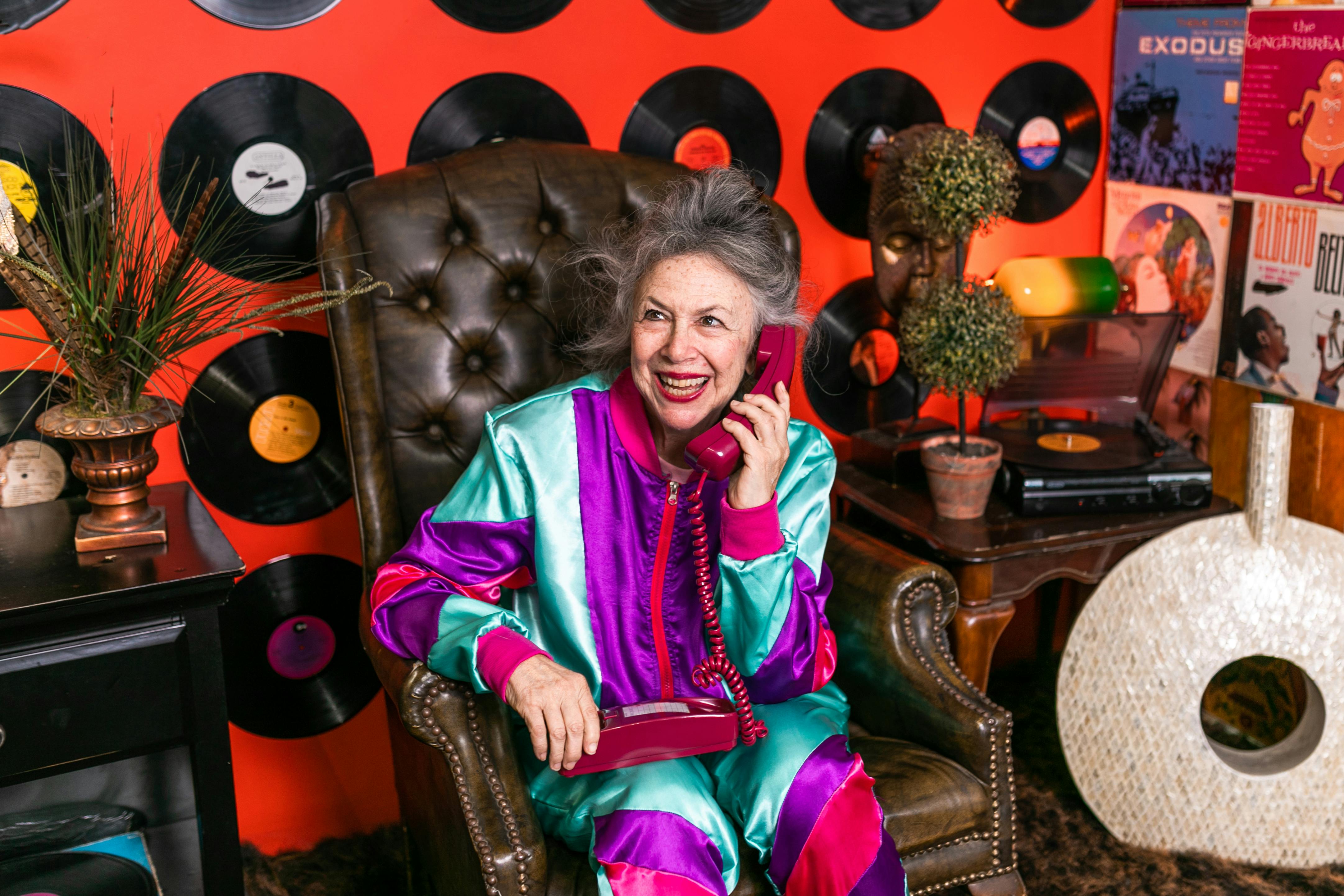 elderly woman using telephone while sitting on a brown leather armchair