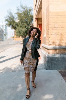 Chic woman in leopard print dress and jacket enjoying a phone call while walking outdoors.