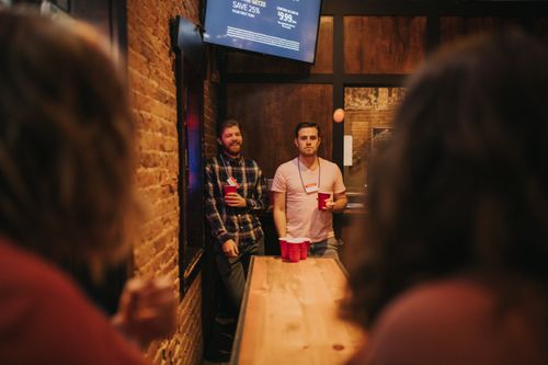 Free Friends playing beer pong in a cozy Denver bar, enjoying nightlife and fun activities. Stock Photo