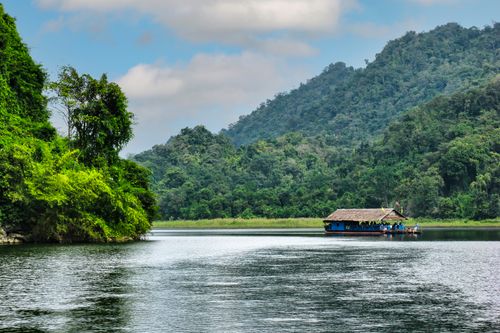 Free Beautiful landscape of a river with a wooden boat surrounded by lush green mountains and rainforest. Stock Photo