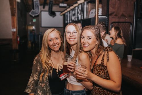 Free Three women smiling and enjoying drinks at a lively bar in Denver. Stock Photo