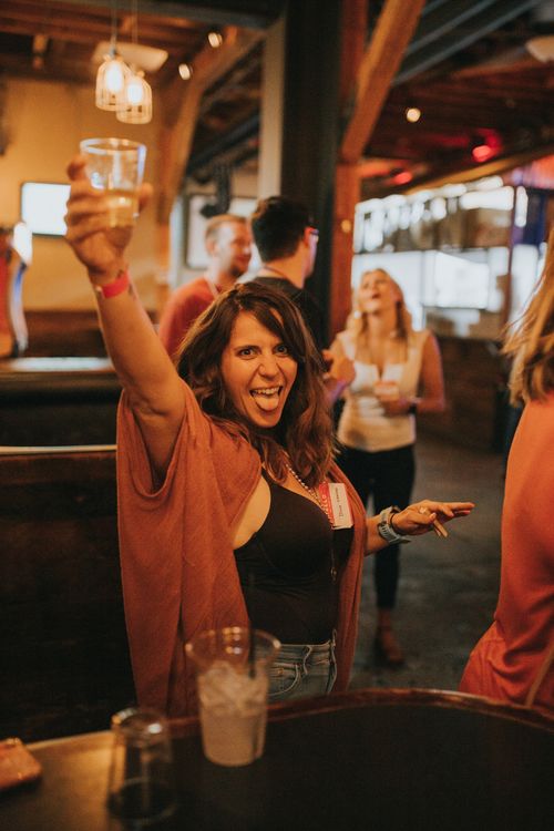 Free Woman enjoying a night out in a pub, raising her drink with a vibrant smile. Stock Photo