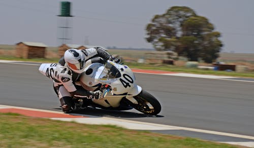 Man in Black and White Motorcycle Suit Riding White Sports Bike on Road