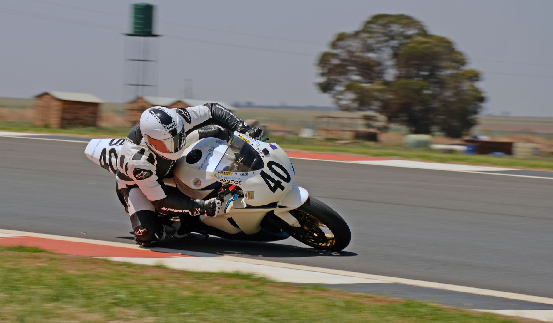 Motorcycle racer leans into a turn on an outdoor asphalt track, showcasing speed and precision.