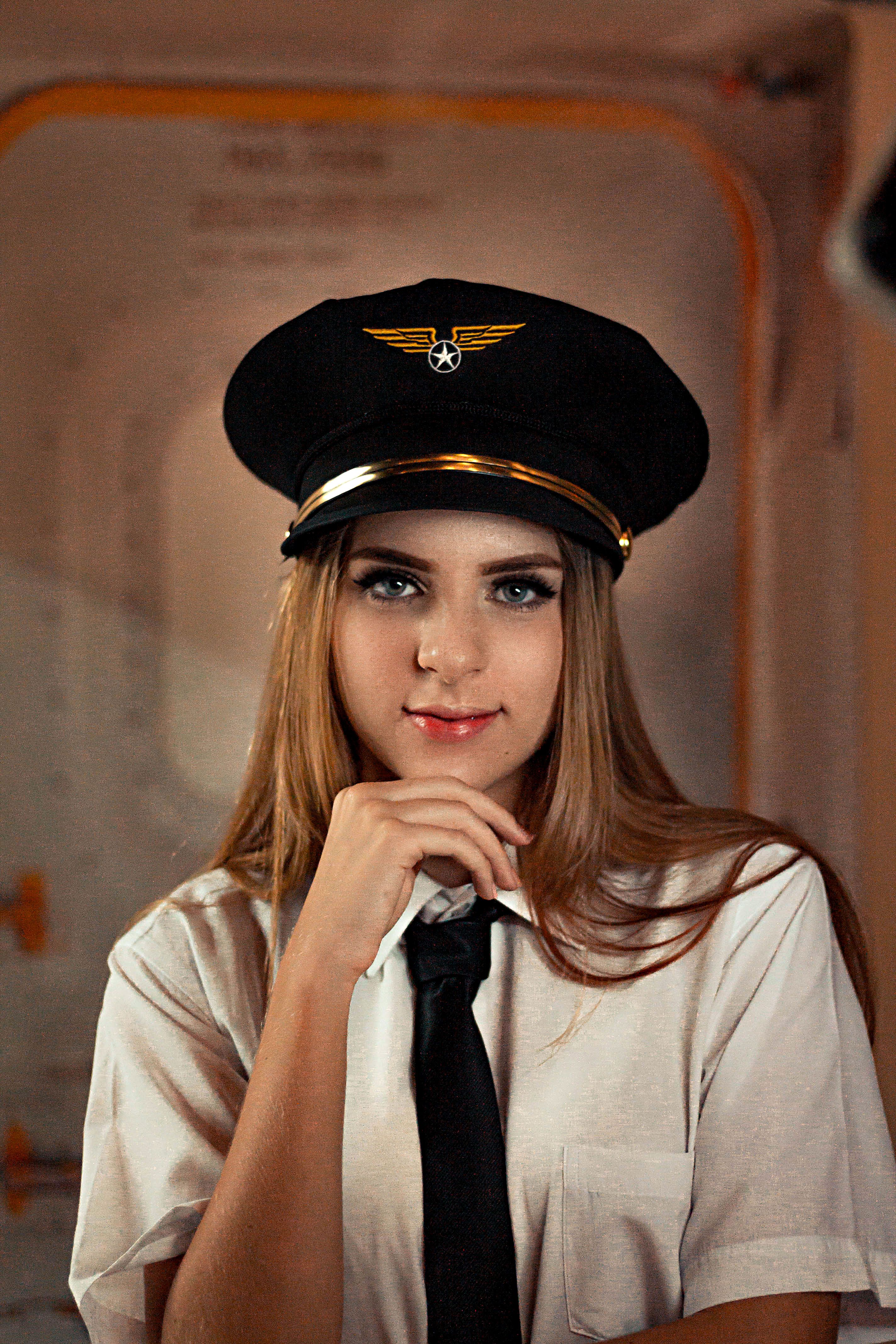 Portrait of a young female pilot wearing a uniform and hat indoors.