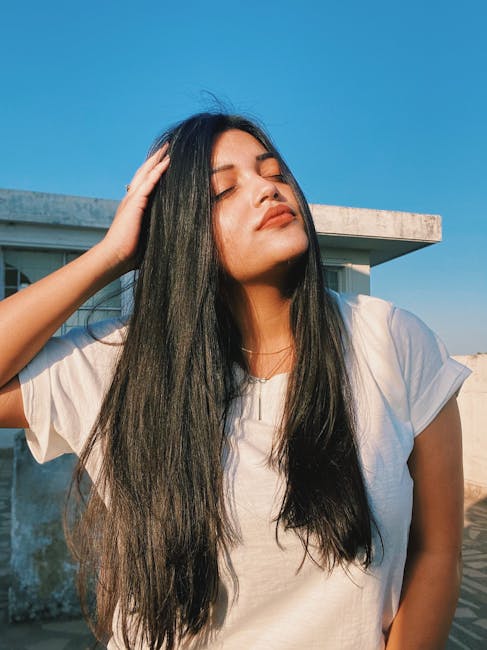 Close-up portrait of a woman with long hair, eyes closed, enjoying sunlight outdoors.