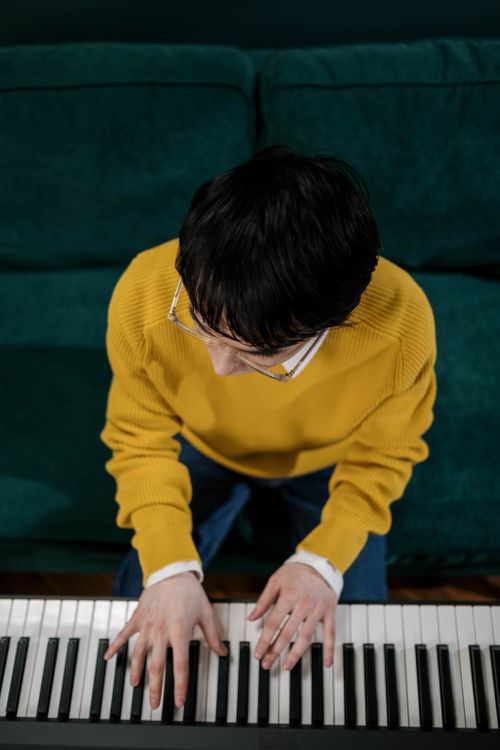 Free A young man in a yellow sweater plays piano indoors viewed from above Stock Photo