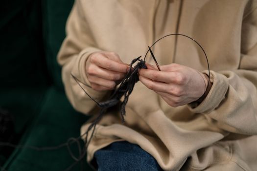 Hands skillfully knitting black yarn, showcasing a cozy indoor hobby.