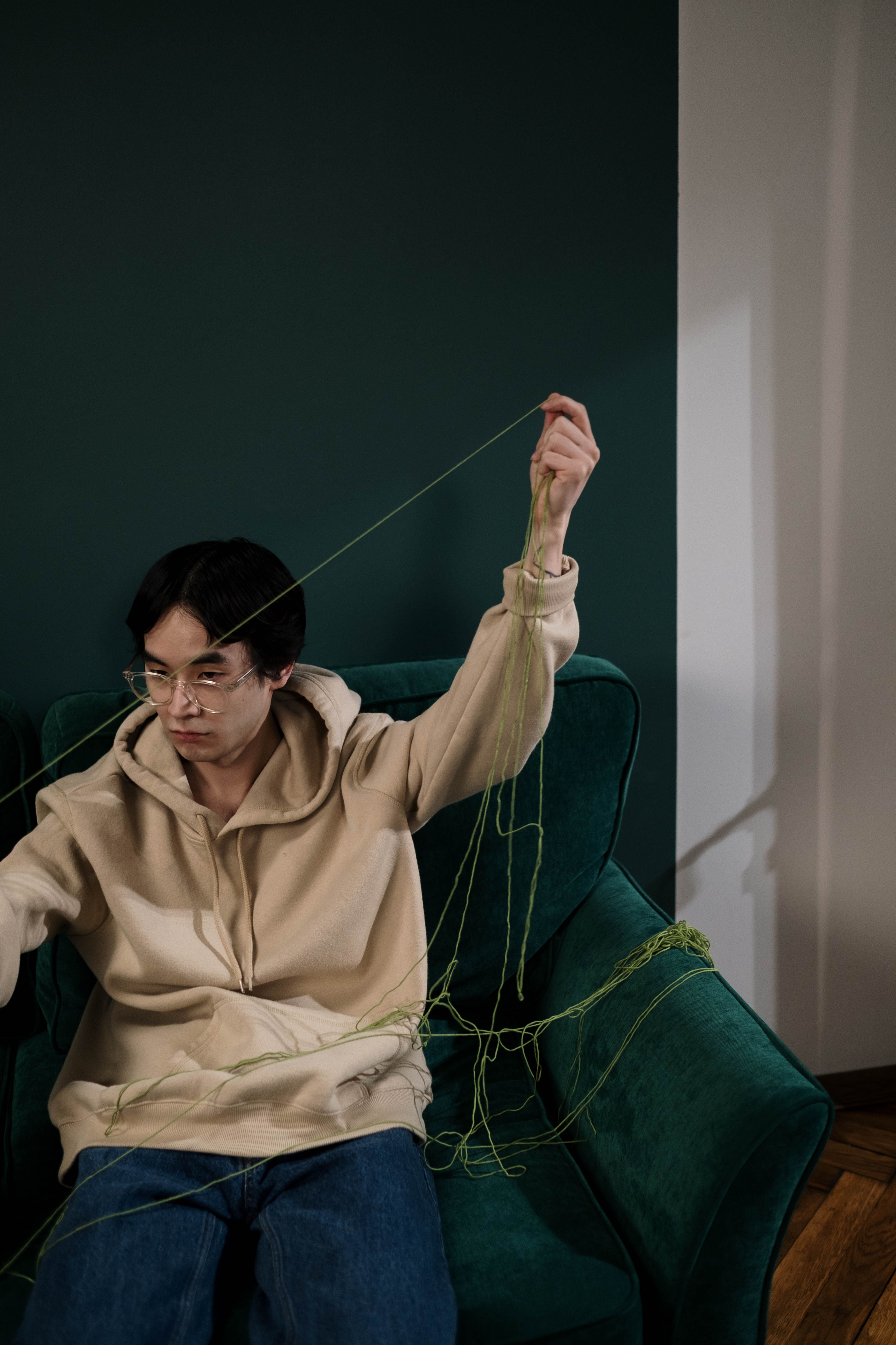 Man Sitting on the Green Sofa Holding a Green Thread · Free Stock Photo