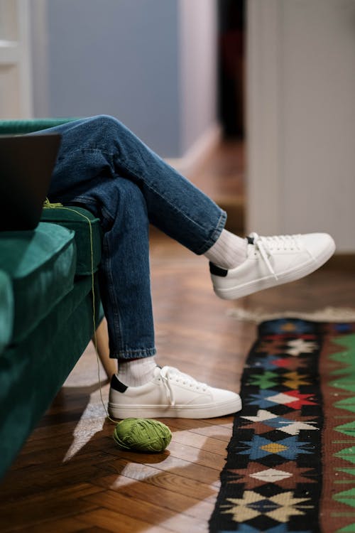 Person in Blue Denim Jeans and White Nike Sneakers Sitting on Green Sofa