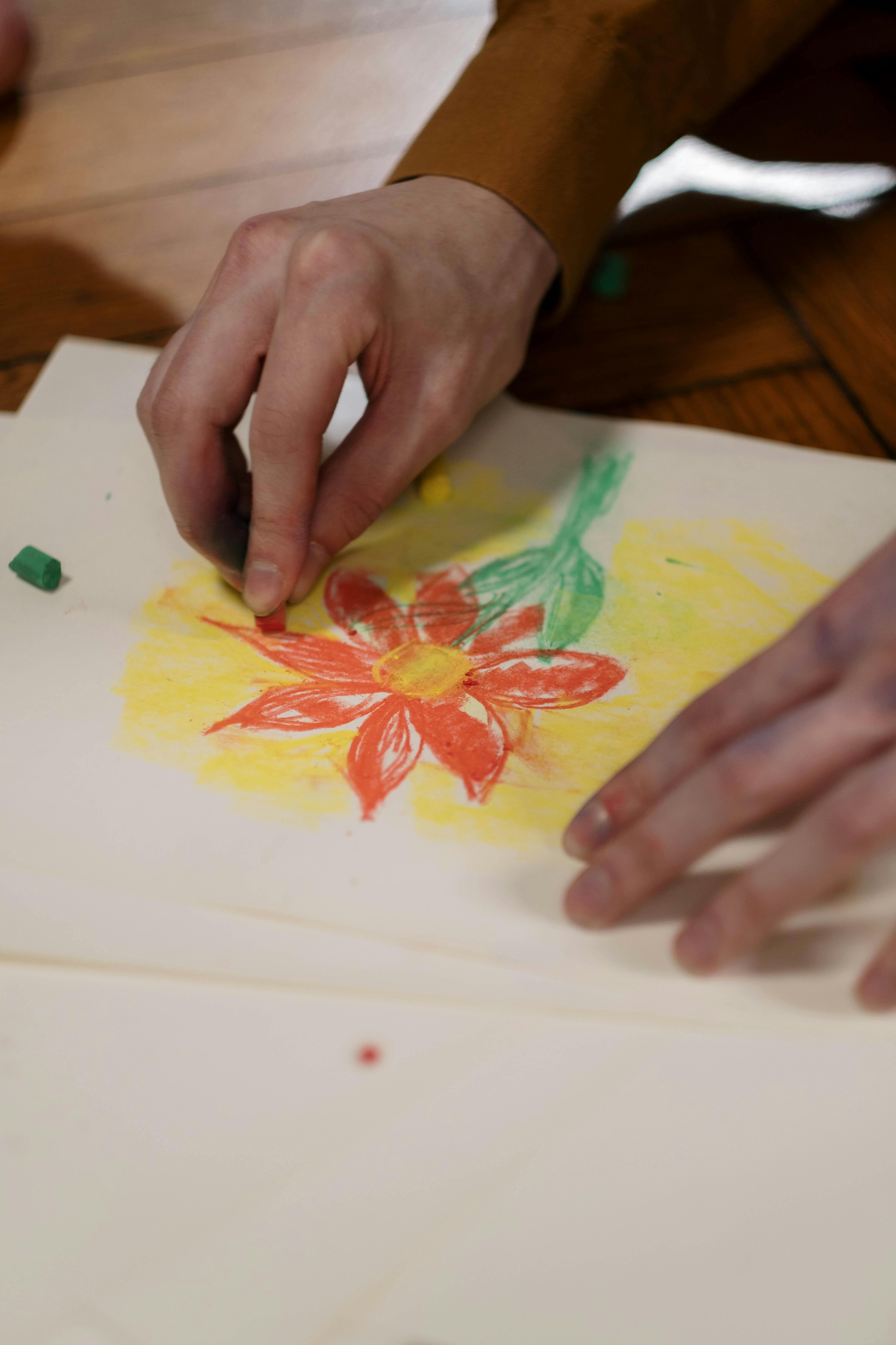 Close-up of hands drawing a vibrant flower with pastels on paper. Perfect for artistic and creative themes.