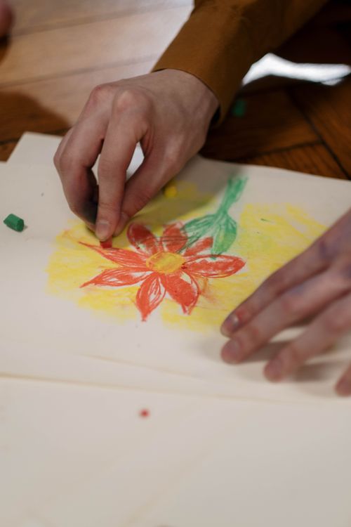 Free Close-up of hands drawing a vibrant flower with pastels on paper. Perfect for artistic and creative themes. Stock Photo