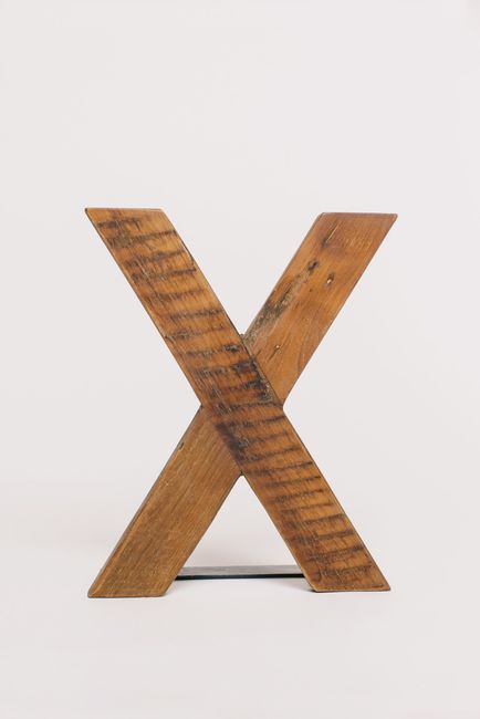 Close-up of a rustic wooden letter X on a simple white background, perfect for design projects.