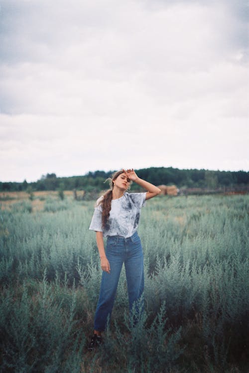 Woman in a Shirt and Blue Denim Jeans Standing on Green Grass Field