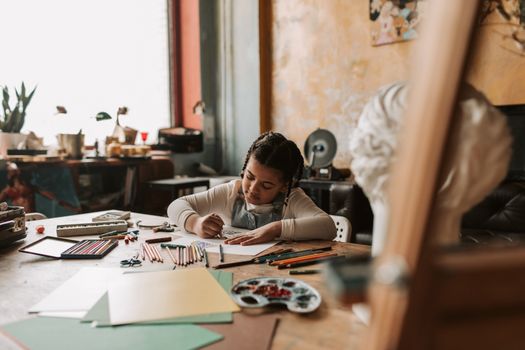 A child engrossed in drawing with colored pencils in a warm, cozy indoor art studio setting.