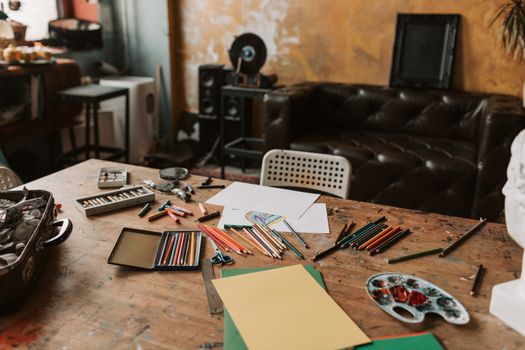 Art studio with colored pencils, paper, and various art materials on a rustic table.