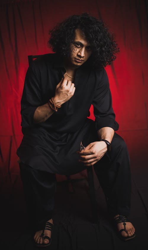 Man with Curly Long Hair Sitting over Red Background