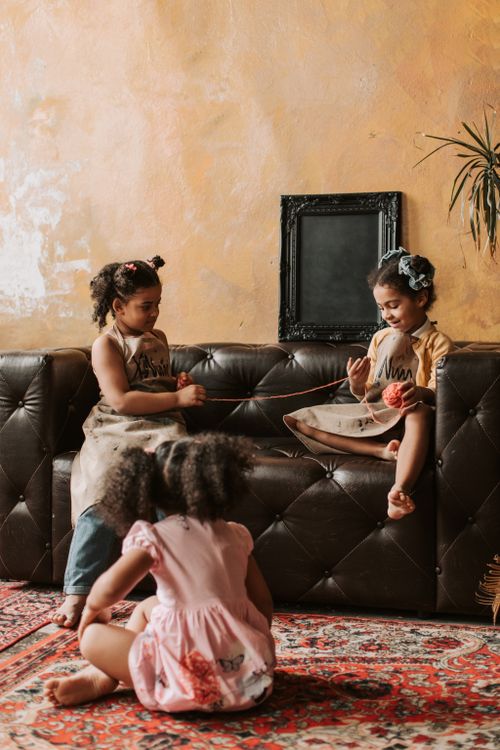 Free Three children engaging playfully with yarn in a cozy living room, fostering creativity. Stock Photo