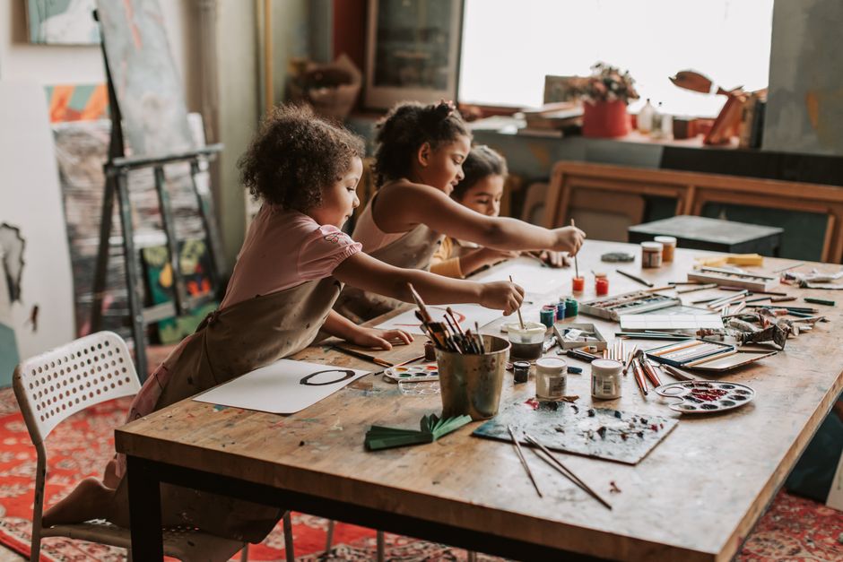 Three young girls engaged in painting at an indoor art studio, exploring their creativity.