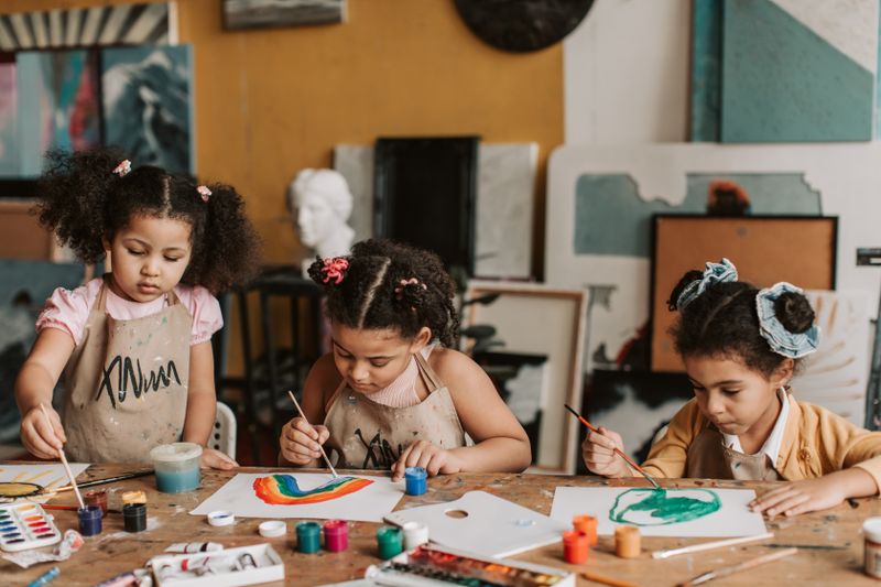 Three children painting creatively at a wooden table in an art class