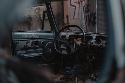 Free Through hole of broken window of damaged old timer automobile with steering wheel and door parked on street with graffiti Stock Photo