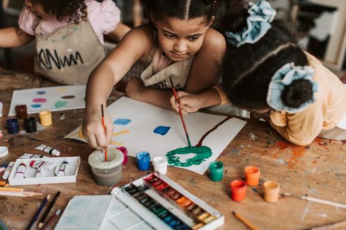 Free Children engaging in a colorful painting session, showcasing creativity and teamwork at an art class. Stock Photo