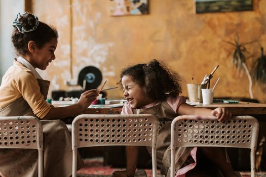 Two African American girls having fun and painting indoors, expressing creativity and joy.