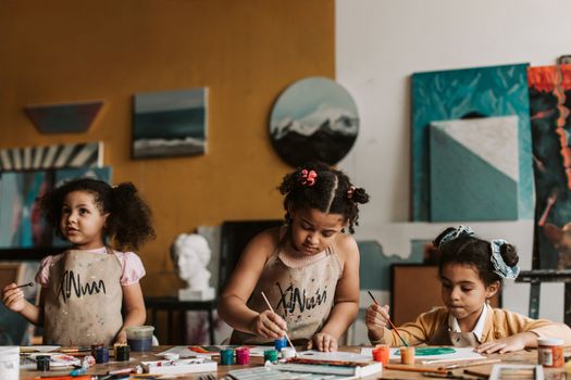 Three young girls painting in an art studio, showcasing creativity and teamwork.