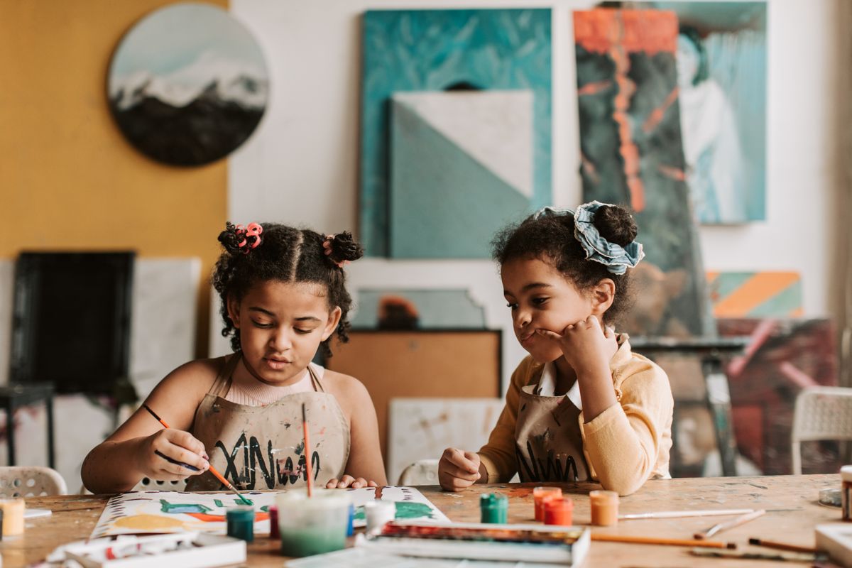 Two young girls painting at a vibrant art studio table