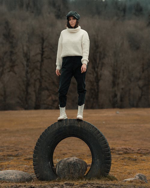 Woman in White Sweater and Black Pants Standing on Black Tire
