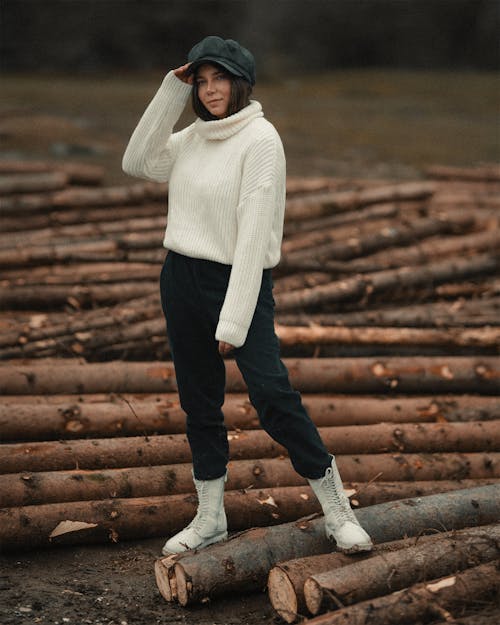 Free Photo of a Woman in a White Sweater Standing on Brown Logs Stock Photo