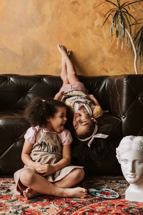 Free Two joyful girls playfully interacting indoors on a sofa, adding warmth and charm to a cozy setting. Stock Photo