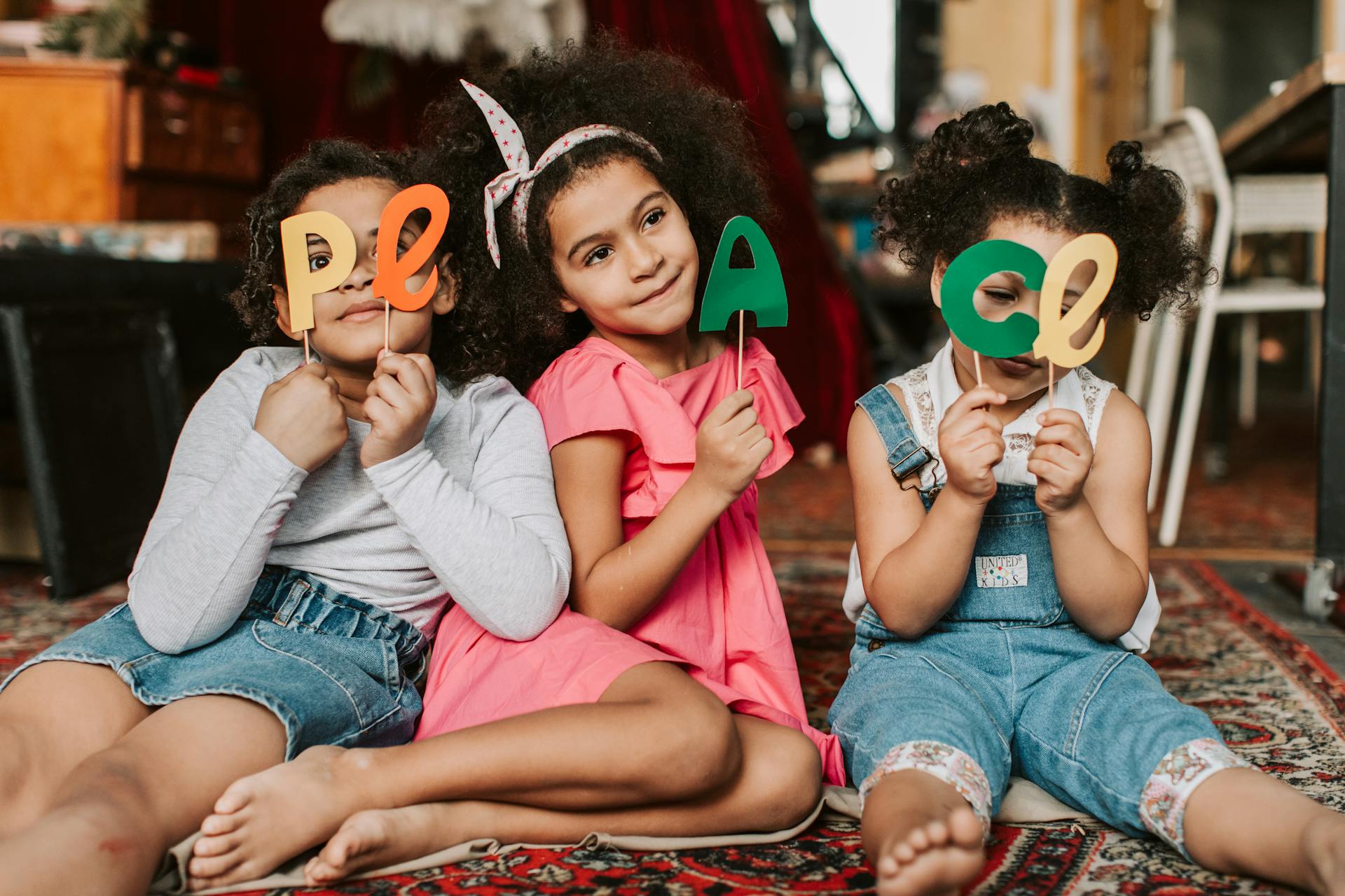 Three children sitting on a carpeted floor, happily holding colorful letter props.