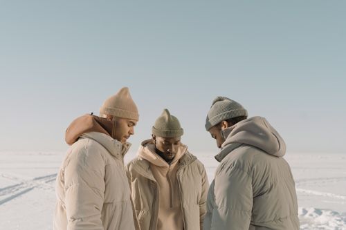 Free Three men dressed warmly in puffer jackets and knit hats stand outdoors on a snowy day. Stock Photo