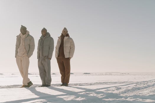 Three men in stylish winter wear posing in a vast snowy landscape.