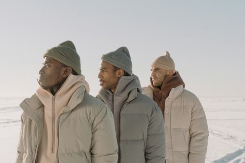 Free Three men modeling winter fashion with puffer jackets and beanies in a snowy landscape. Stock Photo