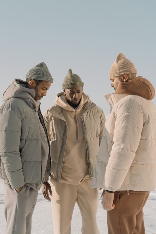 Free Three men in winter clothing featuring stylish puffer jackets and knit hats under clear sky. Stock Photo