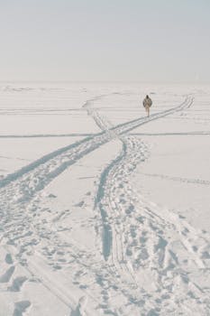A person walking alone on a vast snow-covered field, creating footprints in the winter scenery.