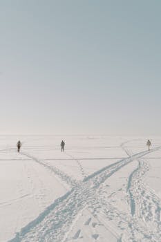 Three people walking across a snow-covered field creating footprints, under a clear winter sky.
