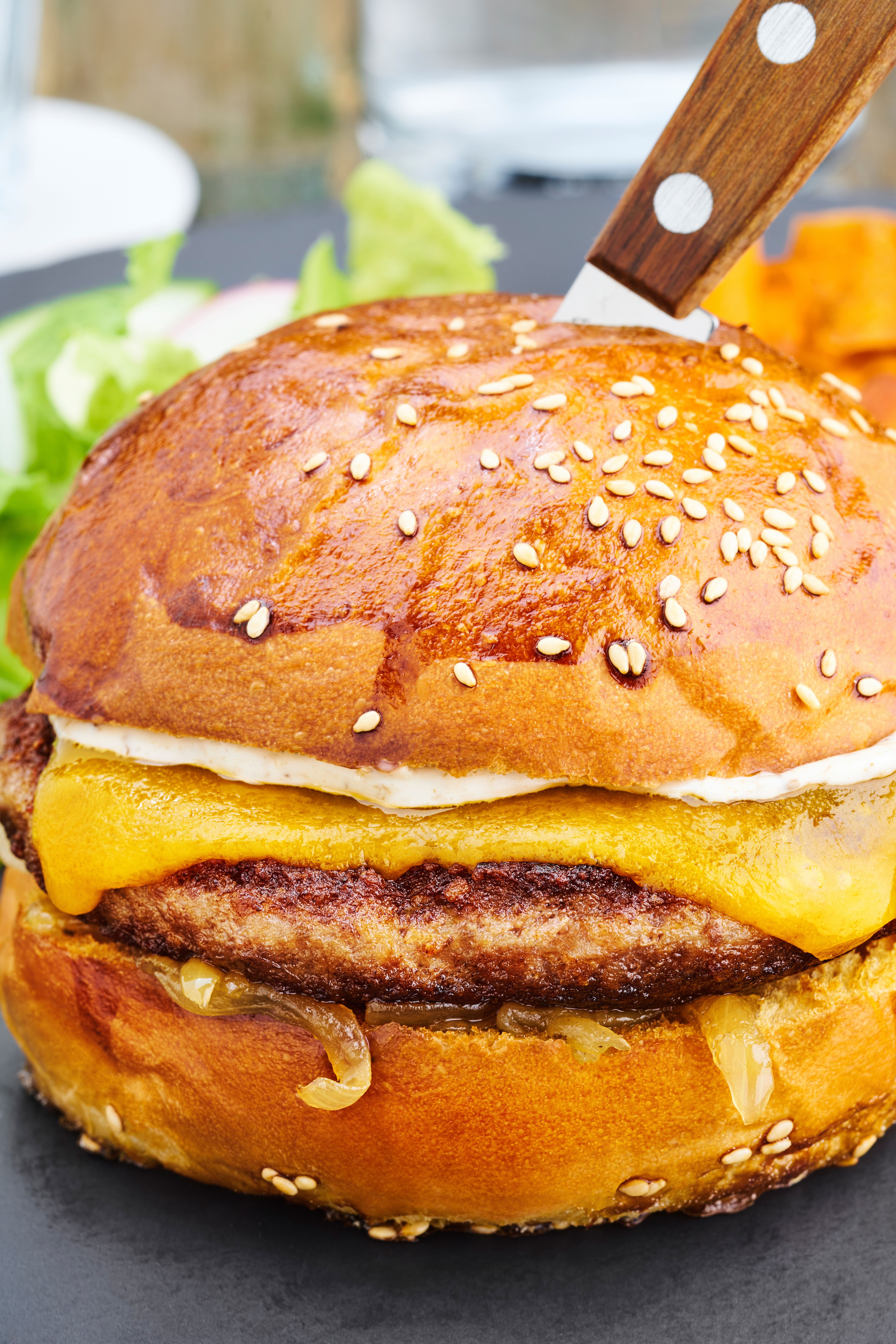 Close-up of a juicy cheeseburger with a knife in a sesame bun, perfect for food photography.