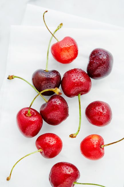Close-up of wet red cherries with droplets on a white surface.