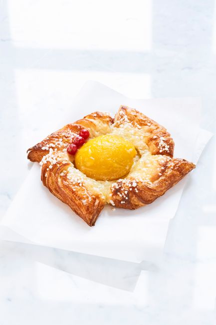 Delicious apricot Danish pastry with icing and fresh ingredients on white background.