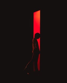 A dramatic silhouette of a person standing against a vibrant red light backdrop, creating a striking contrast.