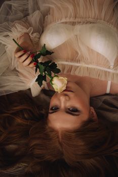 An alluring portrait of a woman lying down, holding a rose, dressed in sheer fabric, exuding beauty and style.