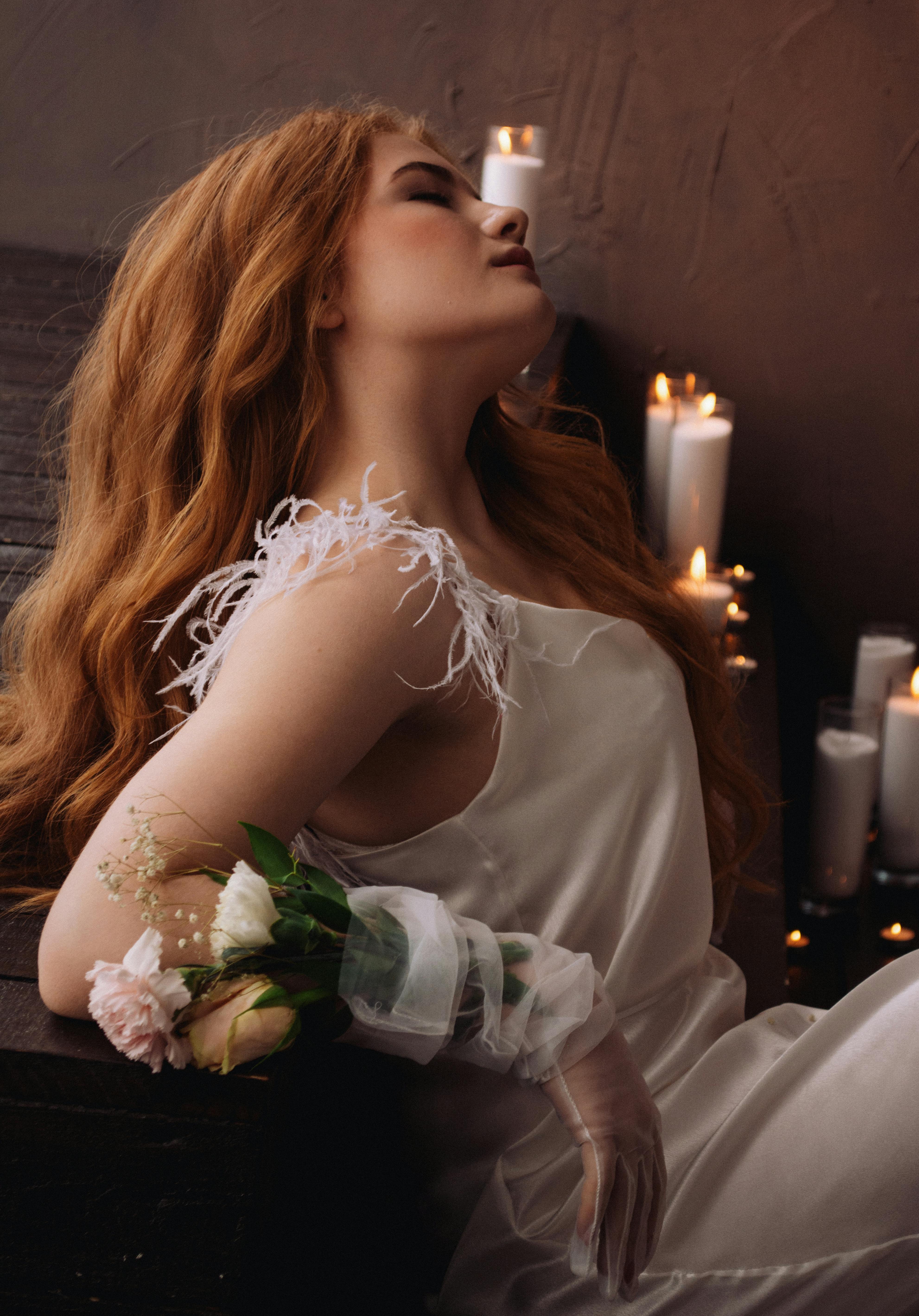 A serene woman in a delicate gown poses with roses amidst a warm, candlelit setting.