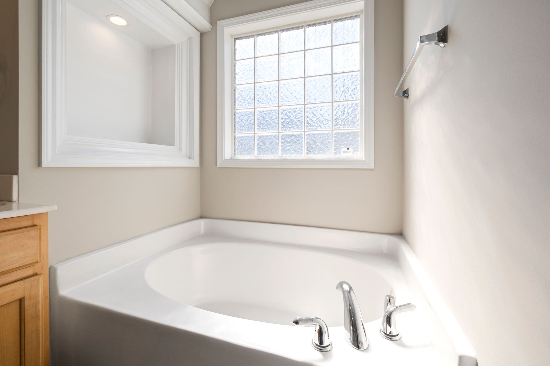 A well-lit modern bathroom featuring a corner bathtub with chrome fixtures and a frosted glass window.