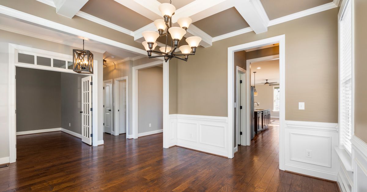 Spacious room showcasing elegant design with hardwood floors, chandelier, and wainscoting.