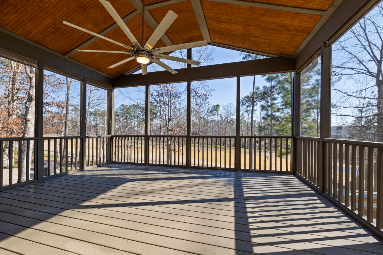 Interior of a screened porch with a ceiling fan overlooking trees