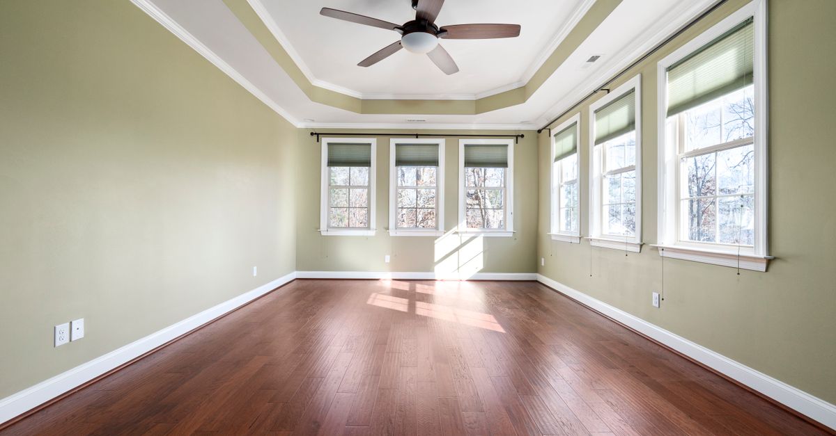 Empty room with hardwood floor, green walls, and large windows providing natural light.